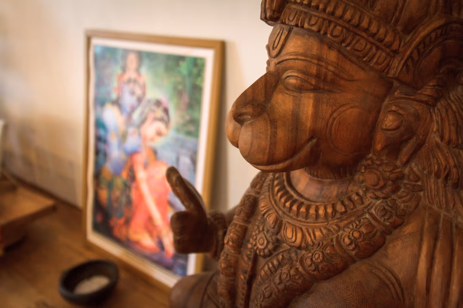 Escultura de madera de Hanuman con pintura de Radha Krishna al fondo